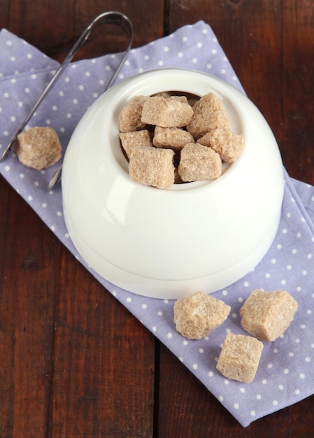 Unrefined sugar in white sugar bowl on wooden background