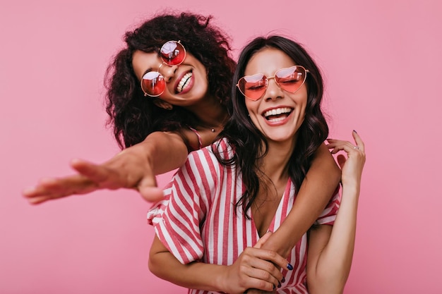 На снимке запечатлено безудержное веселье двух девушек Фото в розовых тонах брюнеток с красивыми локонами, дружески обнявшихся