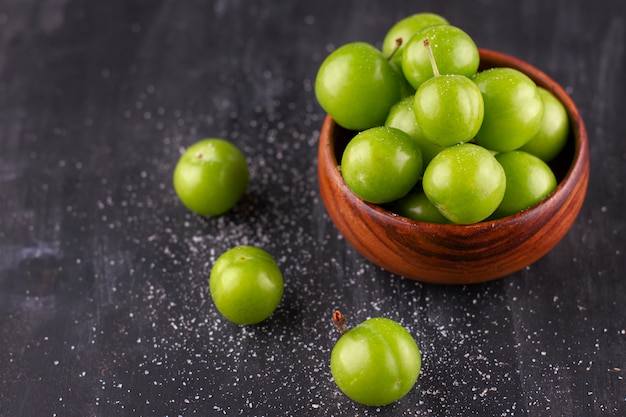 Unripe green plums with salt on a black wooden table