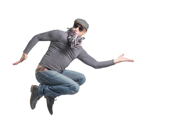 Unshaven bald man wearing a cap jeans sunglasses and scarf jumping Isolated