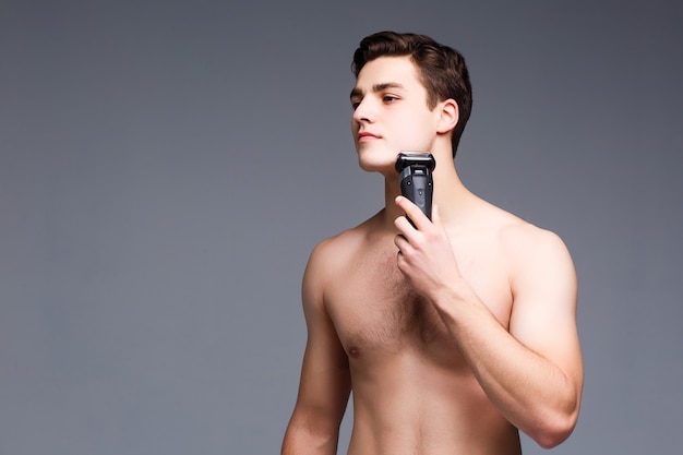 Photo unshaven man with naked torso looking forward to, and using trimmer