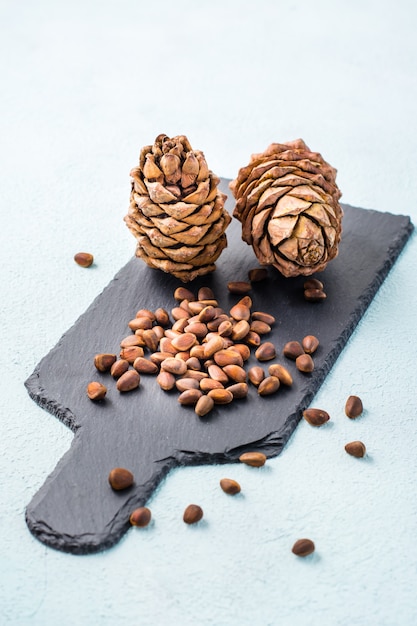Unshelled pine nuts and cones on a slate board. gifts of\
siberia. detox and cure for insomnia. healthy vitamin nutrition.\
vertical view