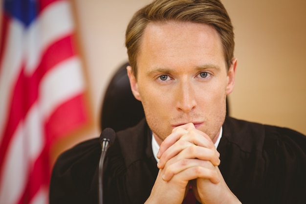 Unsmiling judge with american flag behind him in the court room