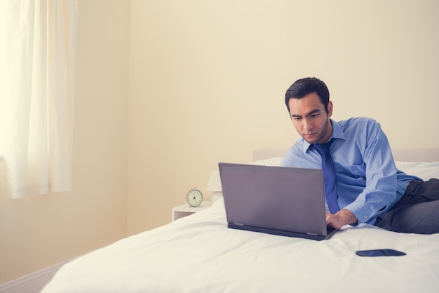 Unsmilingsmens die op een bed liggen die laptop met behulp van