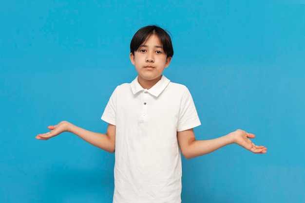 unsure asian boy of twelve years old shrugging his shoulders and don't know on blue background