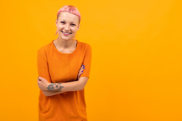 Unusual pretty woman with short pink hair and tattoo smiles isolated on orange