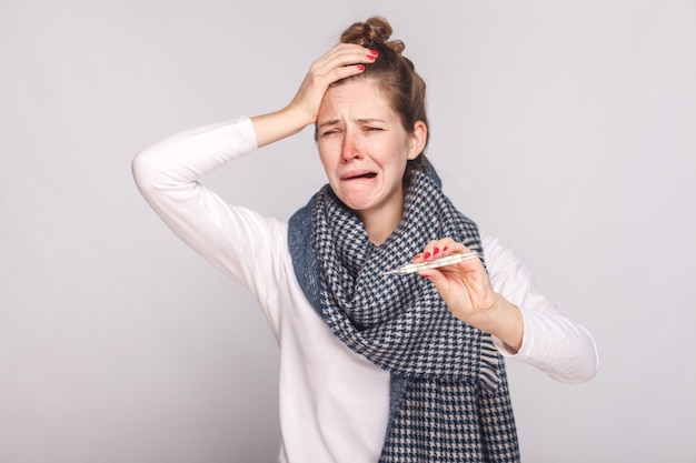 Unwell sick woman have temperature, holding head and cry. Studio shot, isolated on gray background