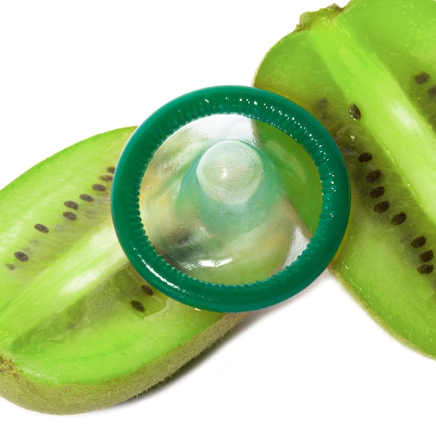 Unwrapped color condom with fruit flavor and kiwi fruit on white background Macro shot