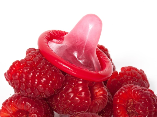 Развернутый цветной презерватив с фруктовым вкусом и малиной на белом фоне