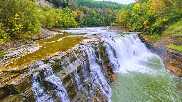 Up close with drone to beautiful waterfall eroding cliffs with colorful forests around