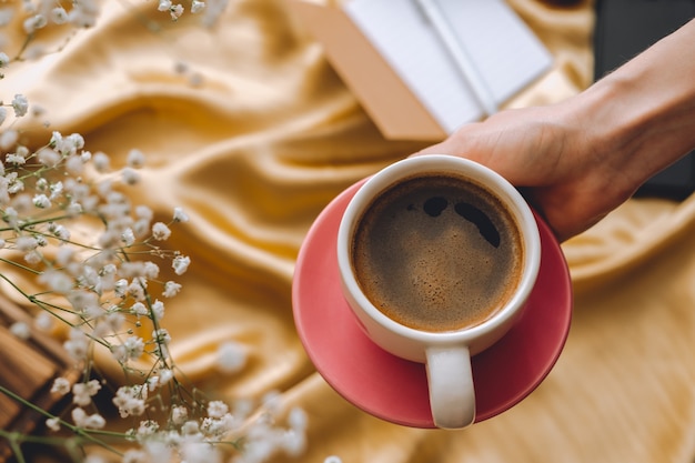 Ð¡up of coffee in hands on a golden satin fabric with gypsophila flowers.