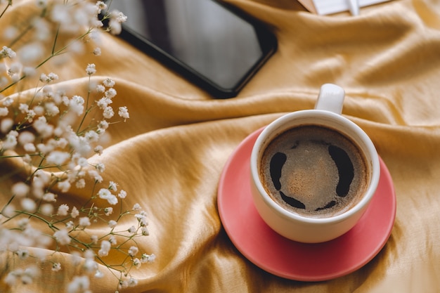 Photo Ð¡up of coffee in hands on a golden satin fabric with gypsophila flowers.