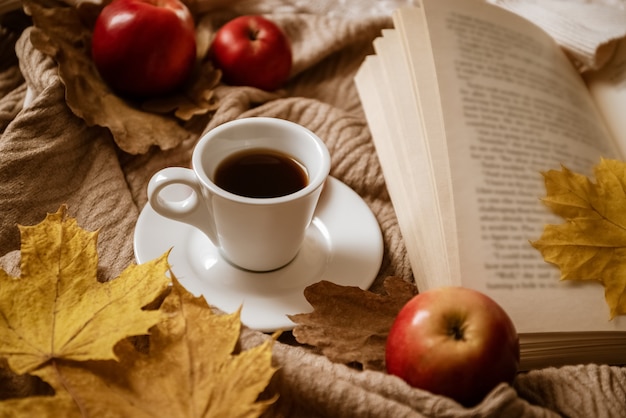 빨간 사과로 둘러싸인 책갈피로 노란 단풍잎이 있는 열린 책 근처에 있는 에스프레소 커피
