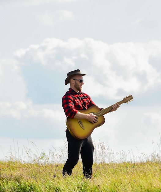 Foto intrattenimento edificante canzone di musica country uomo sexy con chitarra in camicia a scacchi western campeggio ed escursionismo uomo cowboy con chitarrista acustico moda hipster felice e libero