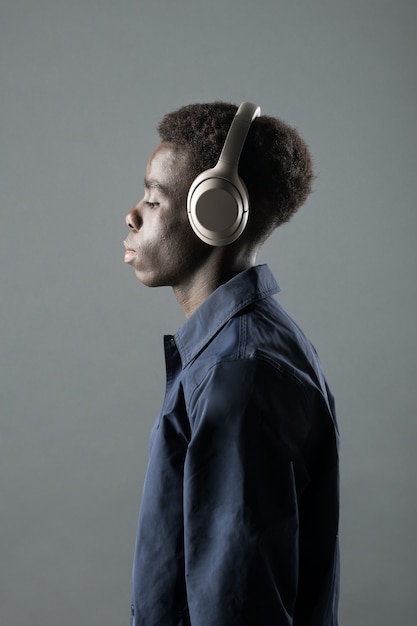 Upper body portrait of relaxed young black man wearing pair of\
headphones, studio background.