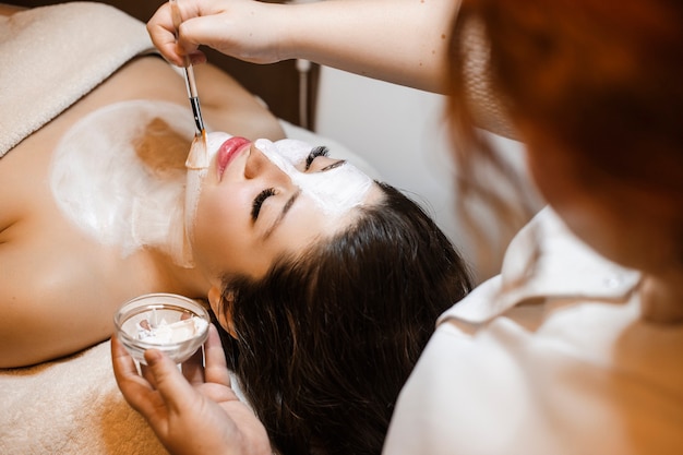 Upper view of a charming young female having facial procedures in a wellness spa center.