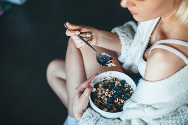 Upper view photo of a caucasian woman in a knitted sweater eating cereals with berry at home