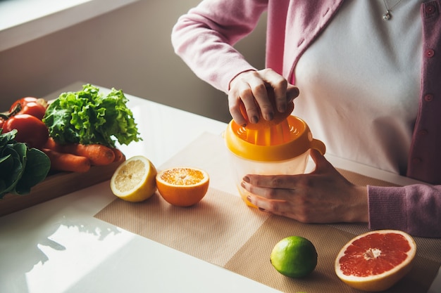 Upper view photo of a caucasian woman squeezing fresh juice from fruits using a squeezer