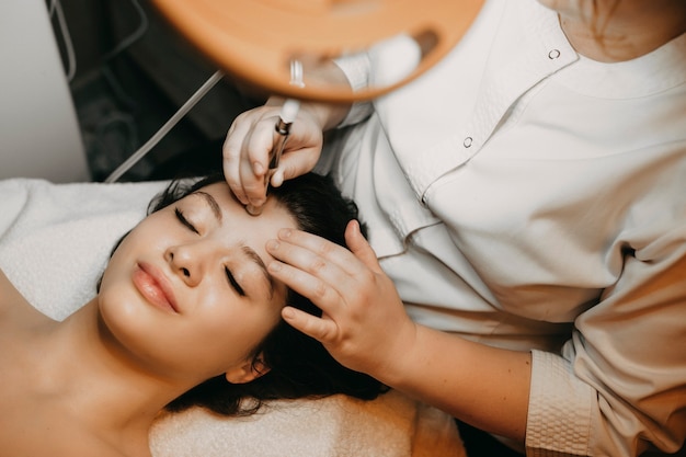 Photo upper view portrait of a lovely female having non invasive microdermabrasion on her face while laying in a spa bed with closed eyes.