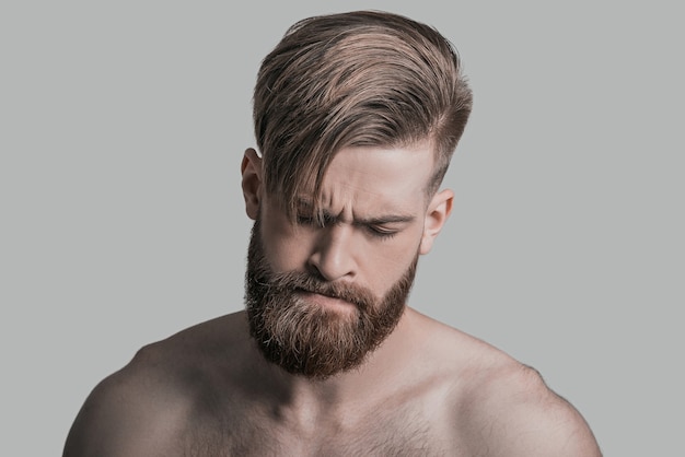 Upset about something. Portrait of young man keeping eyes closed while being in front of grey background