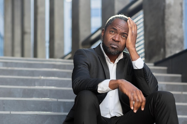 Upset african american man sitting on stairs outside office building businessman bankrupt in despair