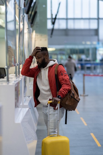 Upset African man standing at checkin counter in airport being sad about moving away