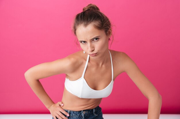 Upset attractive woman in white top and jeans looking at front isolated on the pink wall