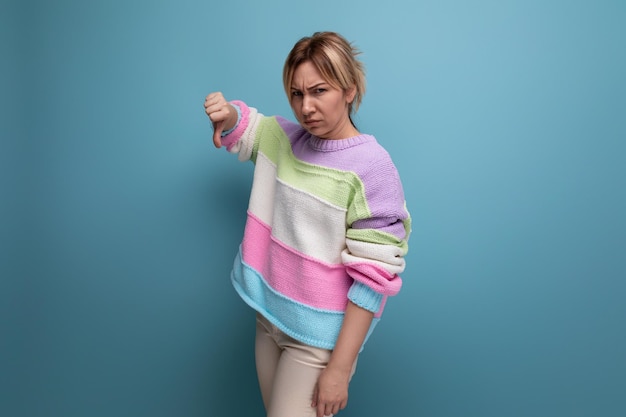 Upset blond woman in a striped sweater shows a dislike on a blue background