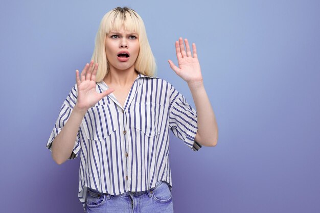 Upset blond young woman in striped shirt on studio background