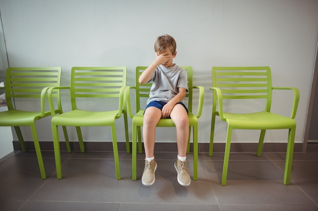 Upset boy sitting on chair in corridor