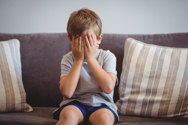 Upset boy sitting on sofa in corridor