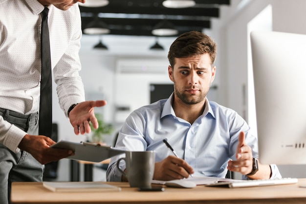 Upset business man having problems with work while sitting by the table in office