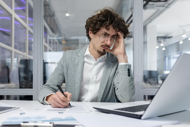 Upset businessman behind paper work inside modern office mature man with beard reading financial