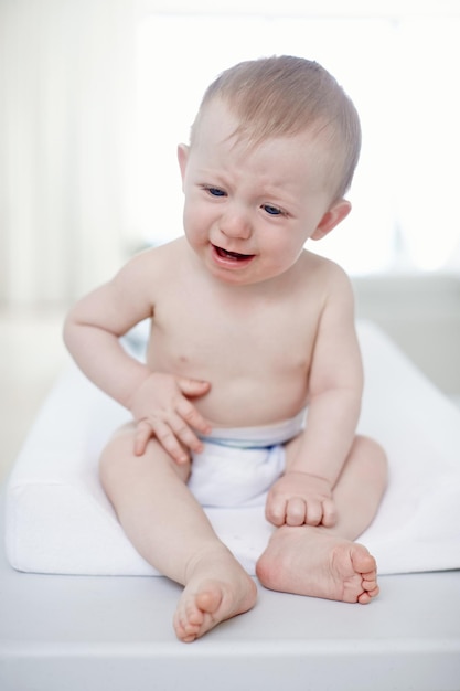 Upset by a tummy ache A crying baby boy sitting on a changing table