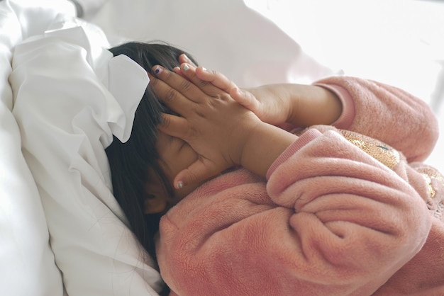 A upset child girl cover her face with hand on bed