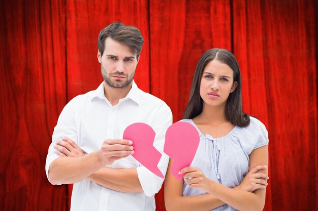 Upset couple holding two halves of broken heart against red wooden planks