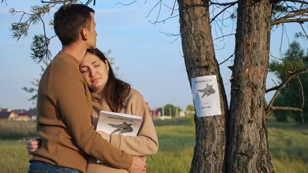 Upset couple hugs in park focus on poster of missing cat