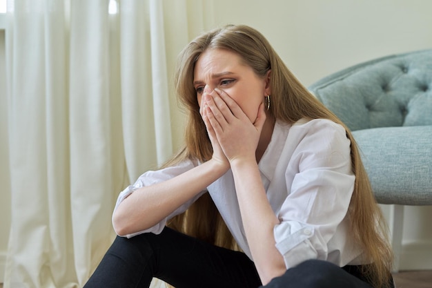 Upset crying young woman sitting at home on the floor