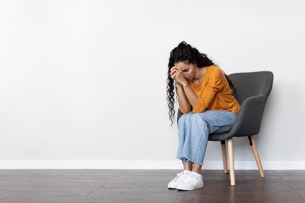 Upset curly brunette woman sitting in arm chair crying