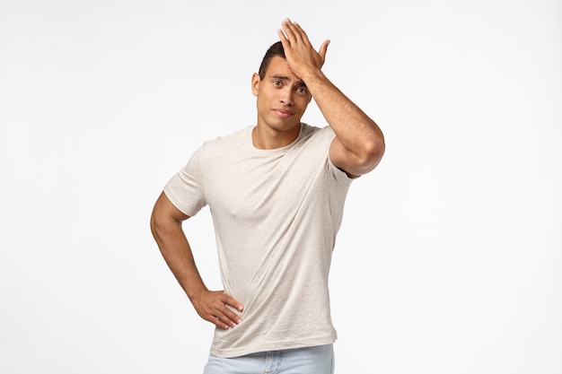 Upset and disappointed gloomy handsome guy in casual t-shirt, punch forehead, facepalm motion, smirk displeased, someone let him down, forgot important task, standing frustrated  