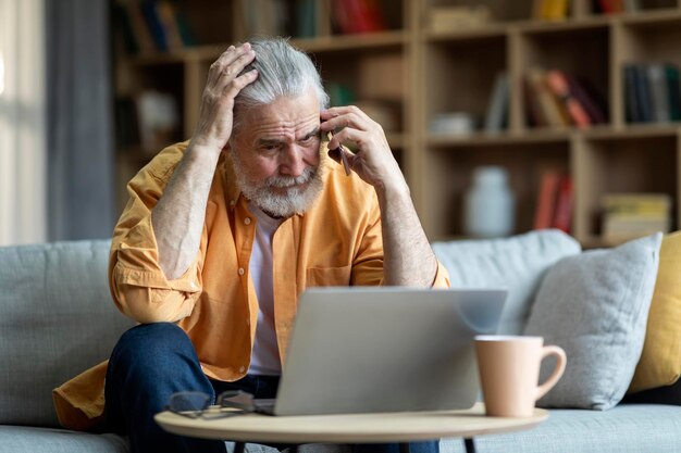 Photo upset elderly man using laptop having phone conversation