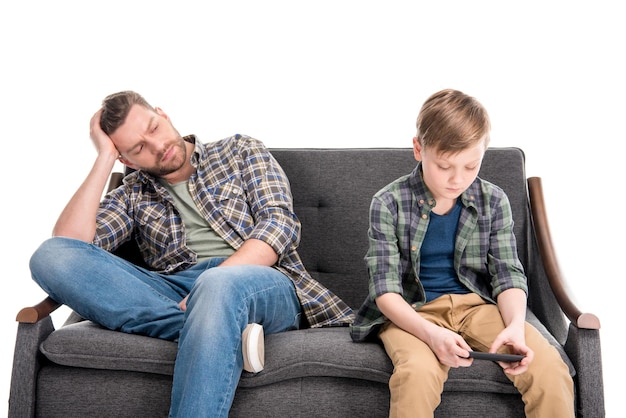 Foto padre sconvolto seduto sul divano e guardando il figlio utilizzando il concetto di problemi familiari dello smartphone