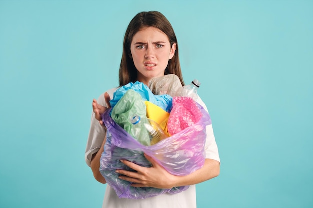 Upset girl holding plastic waste depressedly looking in camera over colorful background isolated