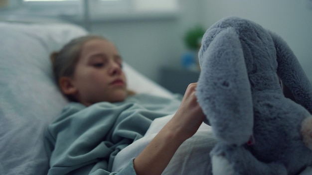 Photo upset girl lying hospital bed portrait sad kid playing with plush toy alone