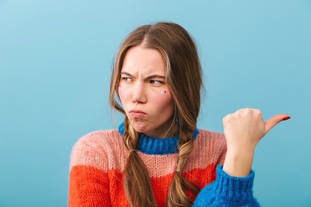 Upset girl wearing sweater standing isolated, pointing away