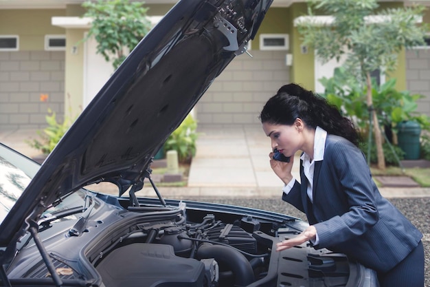 Upset Indian business woman talking on the phone asking for a mechanic help to fix broken down car