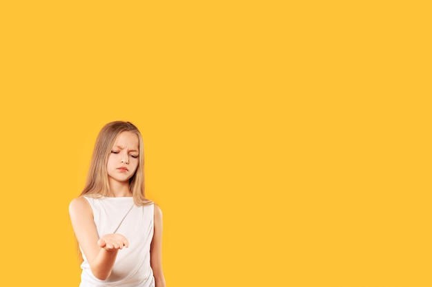 Upset little girl looks at palm outstretched on yellow background