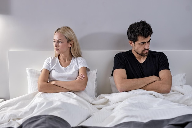 Upset male and female not talking after an argument at home. unhappy couple not speaking after having argument. man and woman in fight with arms crossed sitting on bed after quarrel at home.