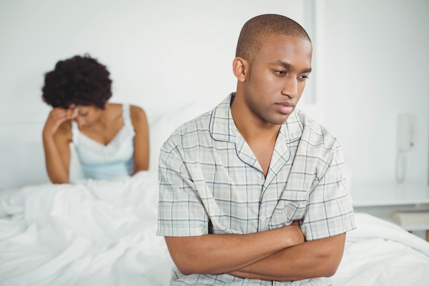 Upset man sitting on bed after arguing with his girlfriend