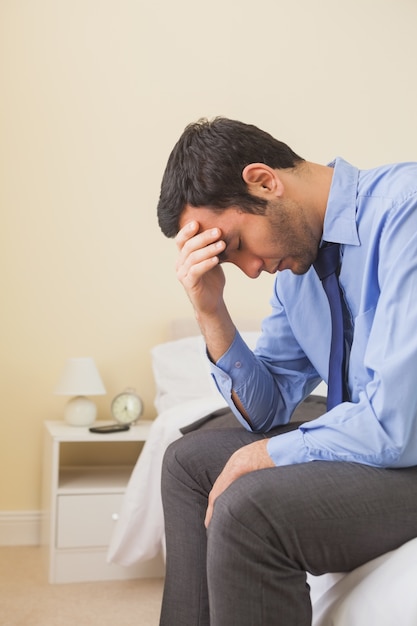 Upset man sitting head in hands on his bed